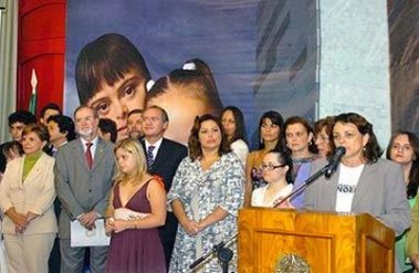 autoridades em palco, com imagem de moça por tras.